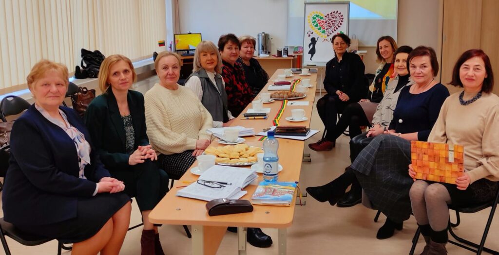 Group of professionals seated around a conference table during a meeting, with notebooks and refreshments visible, discussing ideas in a collaborative environment.