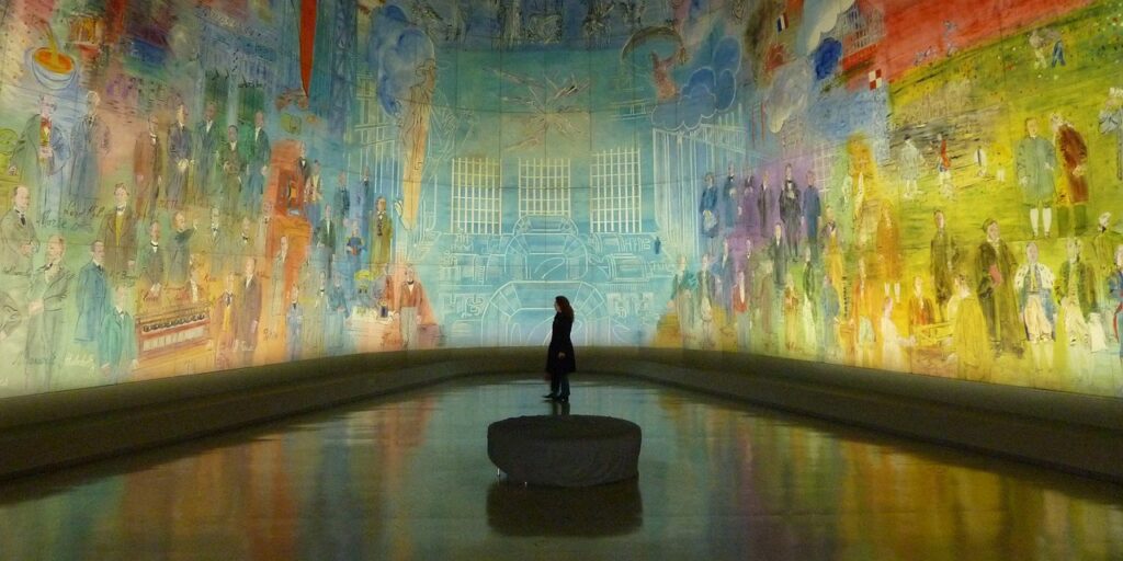 A silhouetted figure stands on a stone pedestal in a vibrant, mural-filled room, showcasing colorful artwork on the walls and a reflective floor, creating an immersive artistic atmosphere.